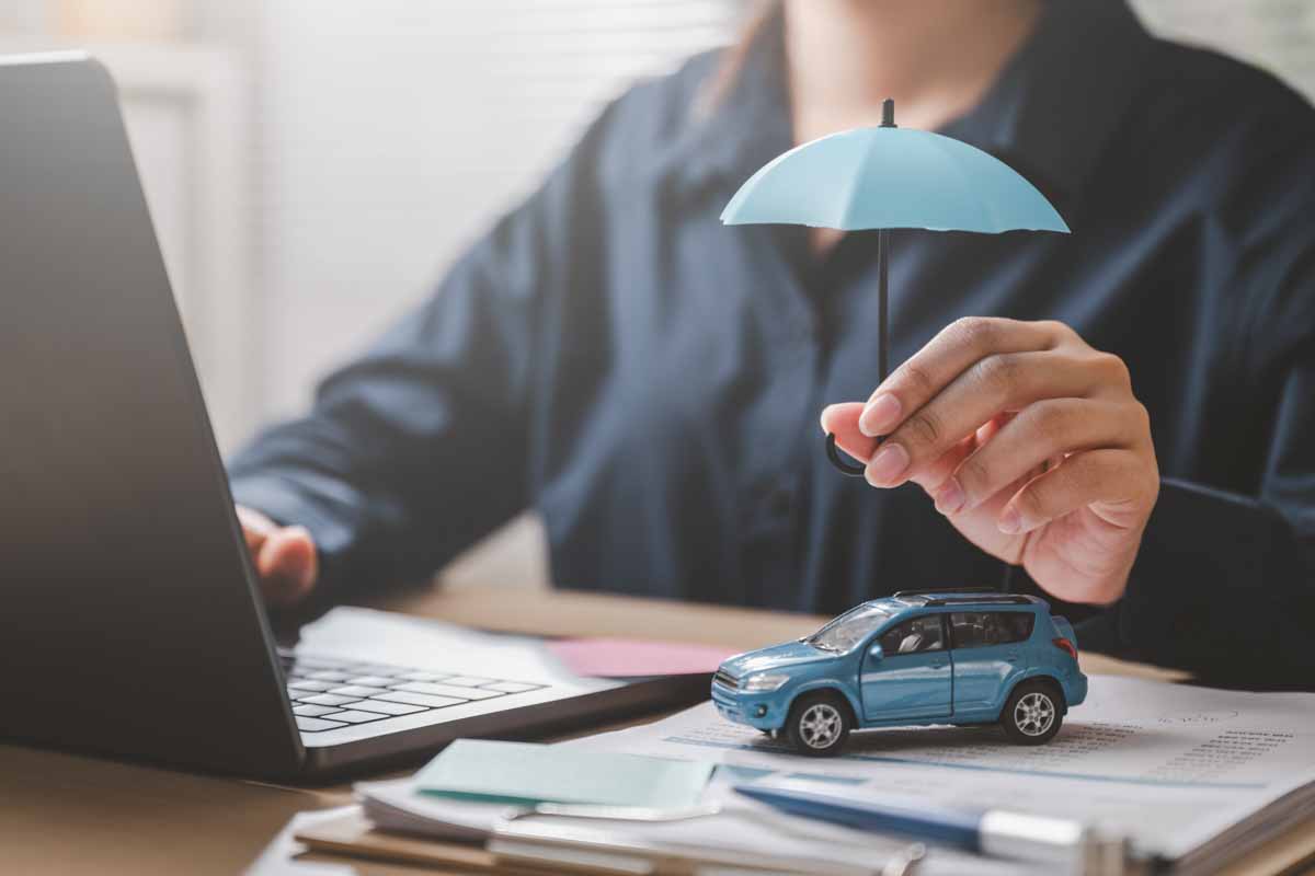 Car insurance protect safe transport. Safety trust. Protection secure assurance. A woman is holding a blue umbrella over a toy car on a desk.