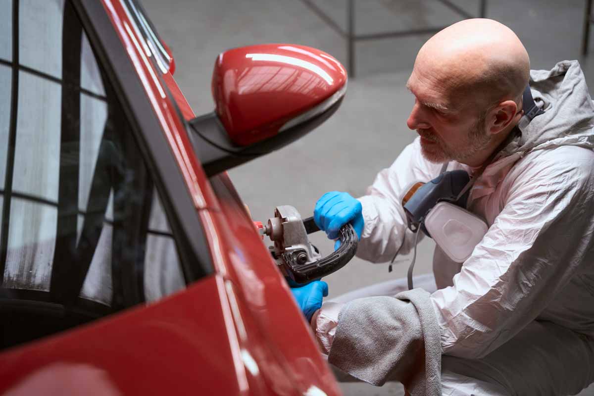 Car repairman at the workplace grinds body of red car