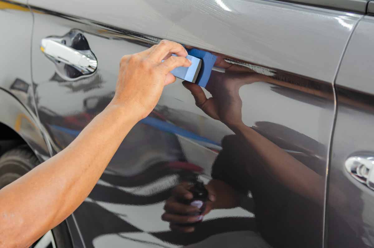 Details of the car. A male mechanic is applying a glass-ceramic coating on the car at the shop.