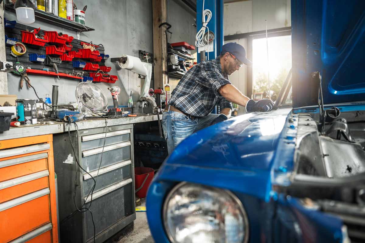 Mechanic Working on Classic Blue Car in Garage Workshop During Daytime